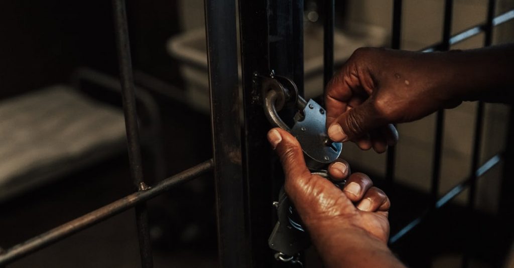 Hands attaching handcuffs to a jail cell door depicting crime and security