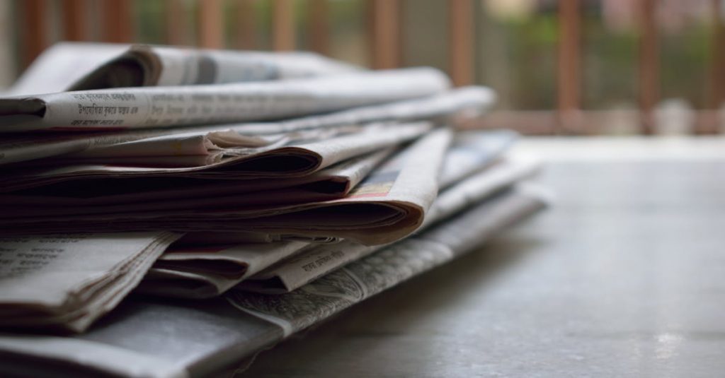 A close-up of a stack of newspapers resting on a desk, symbolizing information and media.